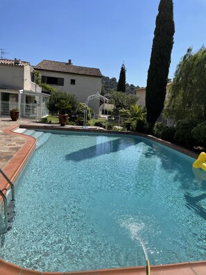 Ein klares Schwimmbecken mit Fliesen umgeben, umrahmt von einem eingezäunten Gartenbereich mit Kübelpflanzen und einer Pergola.