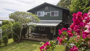 Ein zweistöckiges Haus mit überdachter Terrasse, umgeben von üppiger Vegetation und leuchtenden Blumen.