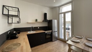 Una cocina moderna con encimera de madera, armarios negros, pileta de acero inoxidable y horno empotrado. Hay un comedor con una mesa para cuatro personas y un ventanal que proporciona luz natural.