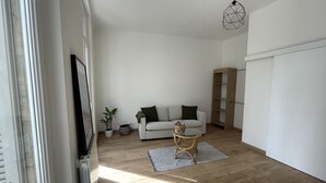 Una sala de estar moderna con un sofá blanco, piso de madera, una mesa de centro de vidrio y una lámpara colgante.