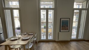 Un comedor con una mesa dispuesta para cuatro personas, ventanas amplias y un cuadro en la pared.