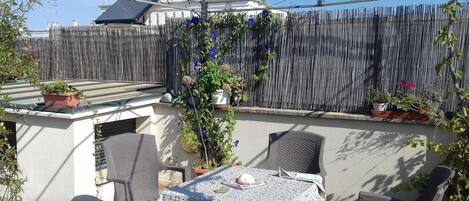 An outdoor patio with a table and chairs, surrounded by potted plants and a bamboo fence.