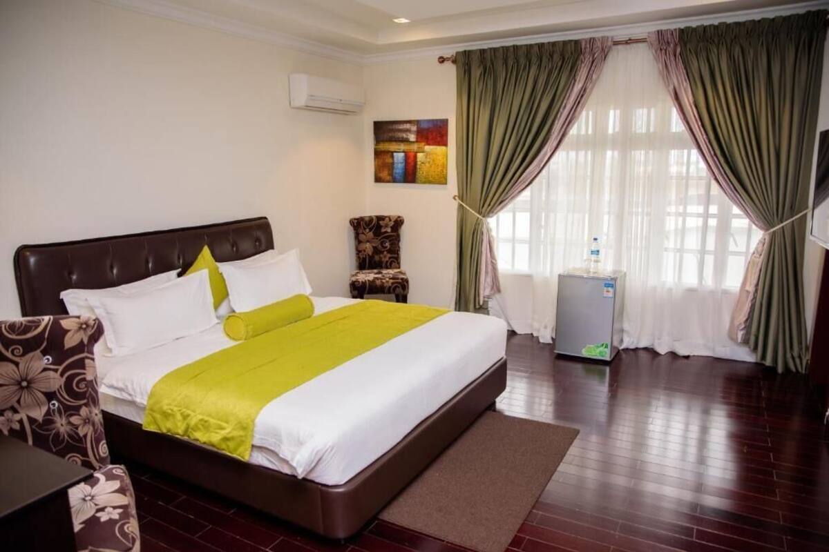 Habitación de hotel con una cama grande, una silla, un escritorio y un refrigerador pequeño.