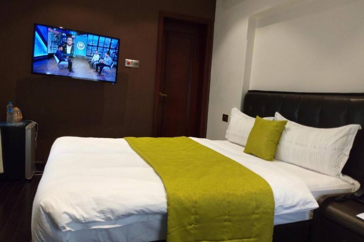 Una habitación de hotel con una cama, un televisor montado en la pared y una puerta.