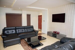 Uma sala de estar moderna com um sofá de couro preto, uma mesa de centro de vidro e uma TV de tela plana na parede.