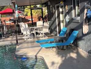 Un área de piscina con sillones reclinables, una mesa y un porche cubierto.
