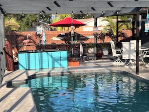 A swimming pool with a hot tub, outdoor seating, and a covered area with string lights.
