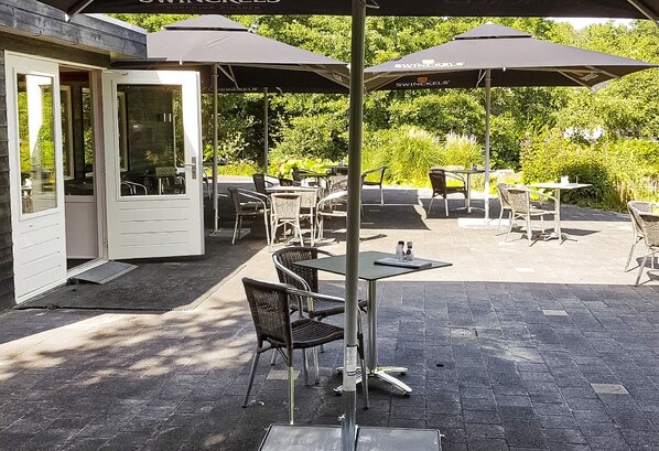 Un espace extérieur aménagé en terrasse, avec des tables et des chaises, des parasols et une porte donnant accès à l’intérieur.