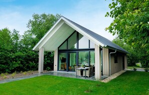 Et moderne hus med stor glasdør, overdækket terrasse og velplejet græsplæne.