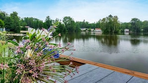 Una terrassa de fusta amb vista a un llac tranquil, amb arbres i edificis al fons.