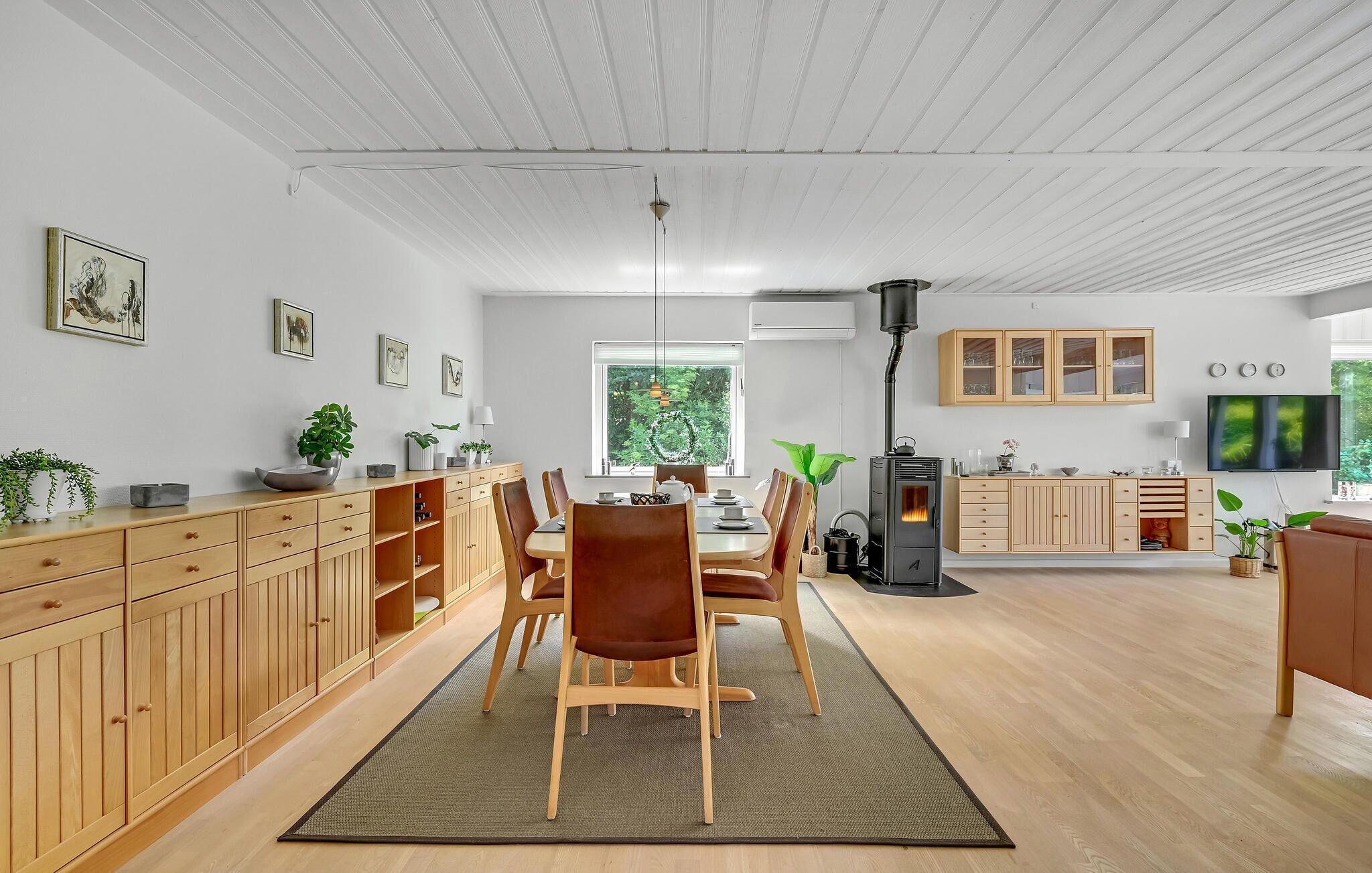 A spacious living area with a dining table, chairs, a fireplace, wooden cabinets, and a television.