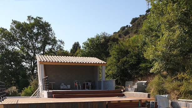 A clear blue pool with wooden deck and steps leading to a covered area with outdoor furniture.