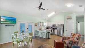 Un amplio espacio de sala con una mesa de comedor, sillas, un sillón colorido a rayas, un otoman tejido y una cocina con barra.