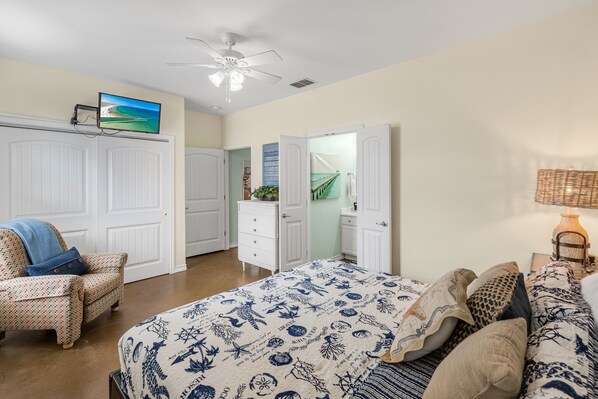 A bedroom with a bed, a chair, a dresser, a television on the wall, and a ceiling fan.