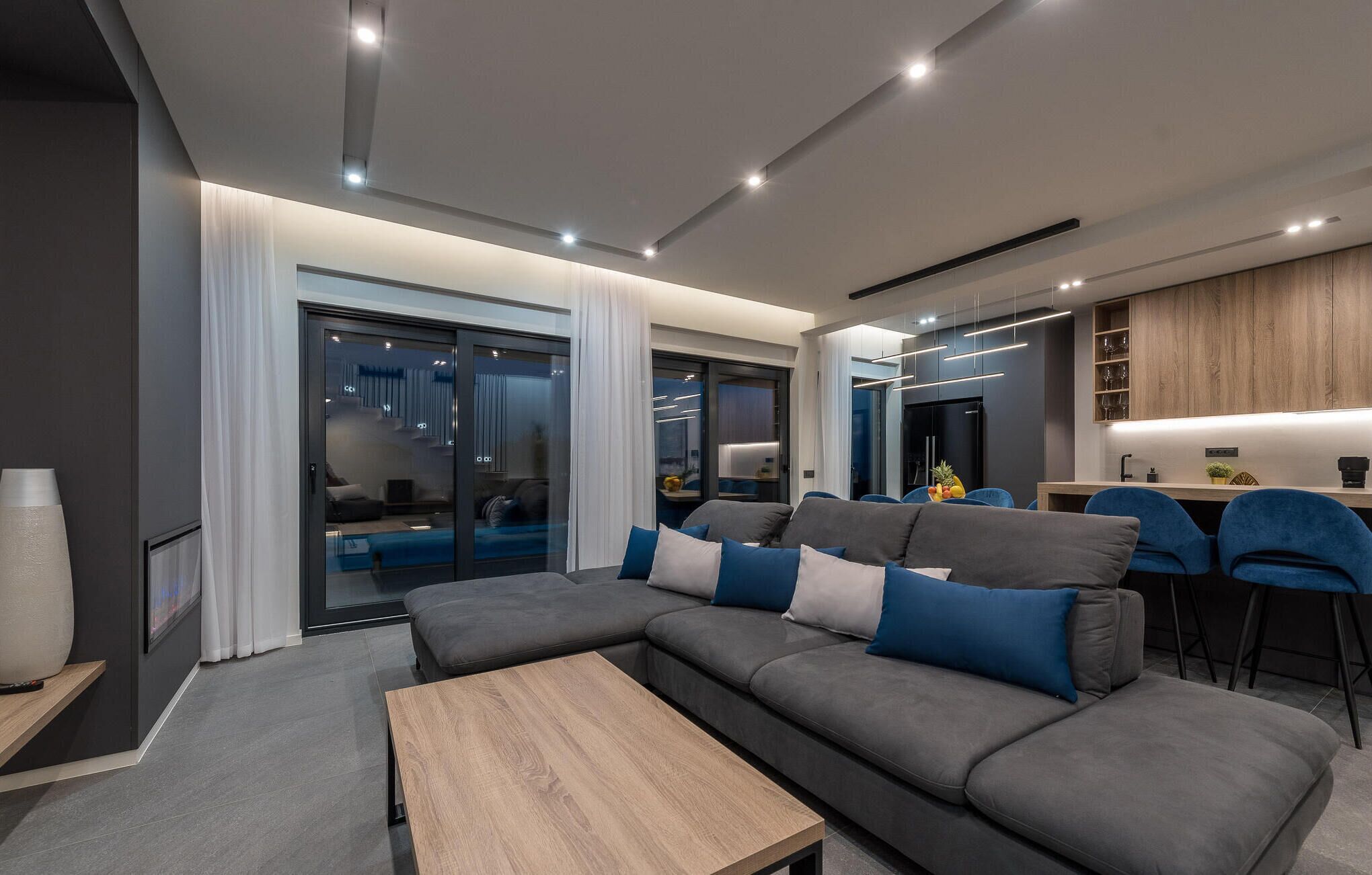 Een moderne woonkamer met een grijze modulaire bank, een houten salontafel en een glazen deur naar een eetgedeelte.