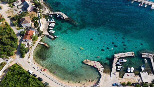 An aerial view of a coastal area with clear turquoise waters, a curved beach, and a marina with boats. - Luxurious home in Lun with sauna (Lun)