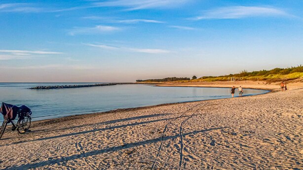 Una playa arenosa con un mar tranquilo, una bicicleta y algunas personas caminando.