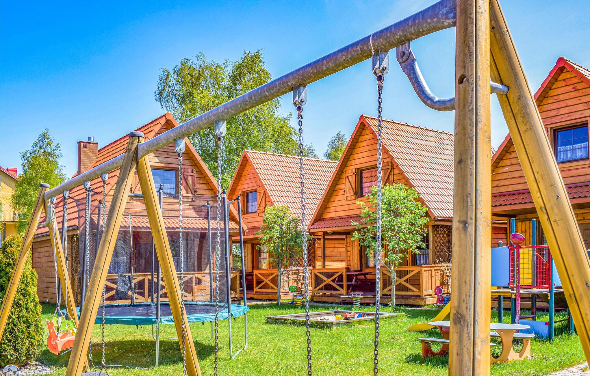 Een speeltuin met schommels en een trampolaan, omgeven door houten huizen met rode daken.
