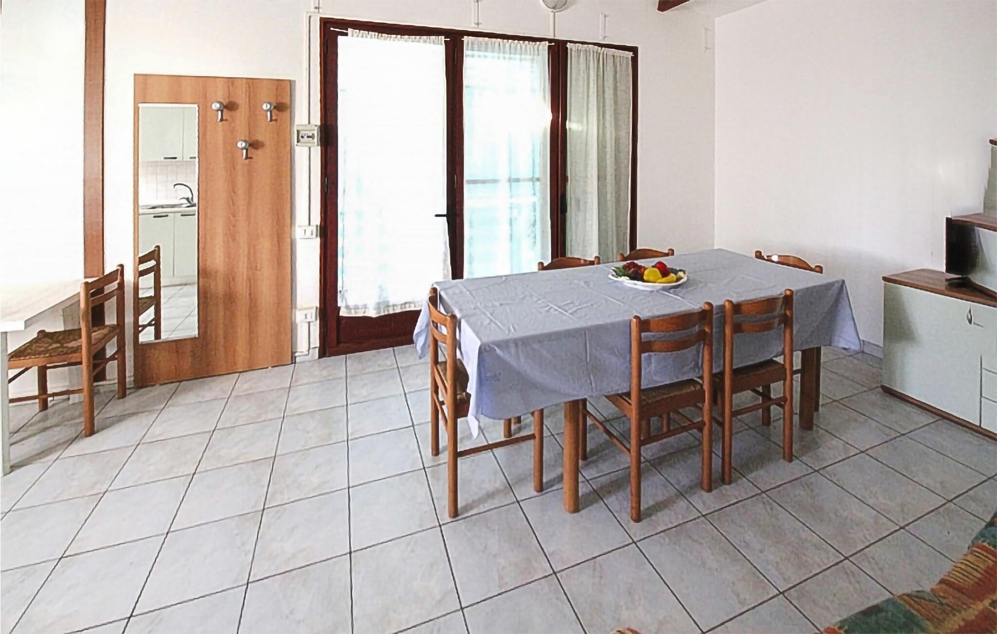 A dining area with a table set for four, a small kitchen area with a TV, and a sliding glass door leading to a balcony.