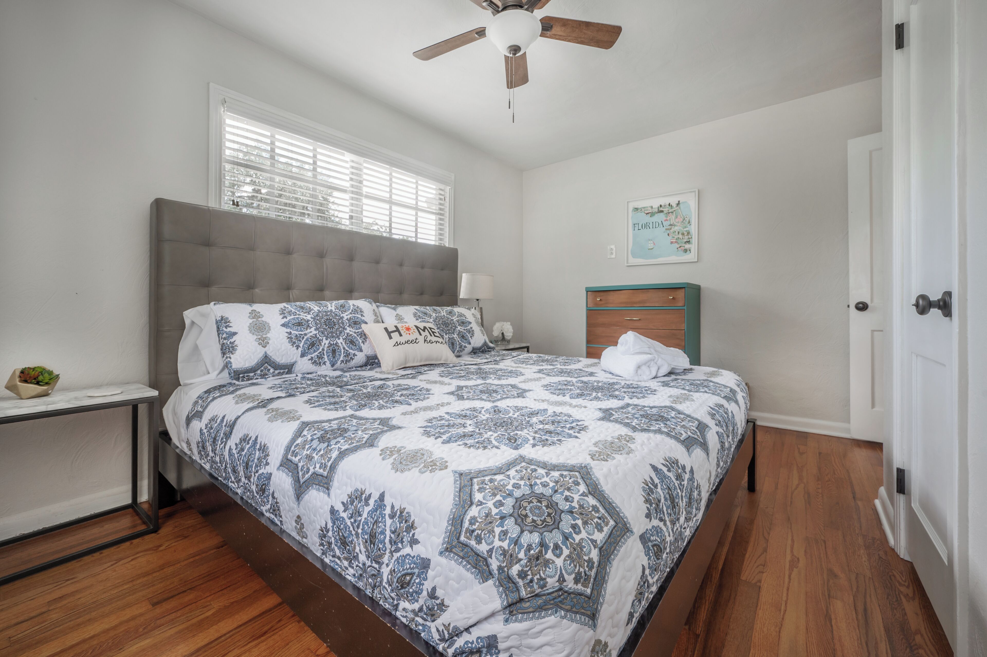 A bedroom with a bed, a nightstand, a dresser, a ceiling fan, and a window with blinds.