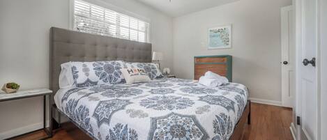 A bedroom with a bed, a nightstand, a dresser, a ceiling fan, and a window with blinds.