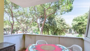 Ein Balkon mit Tisch und Stühlen, mit Blick auf einen Garten mit Bäumen und einem Gebäude im Hintergrund.