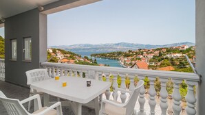 En balkon med et hvidt bord og stole, der giver udsigt over en kystby og bjerge.