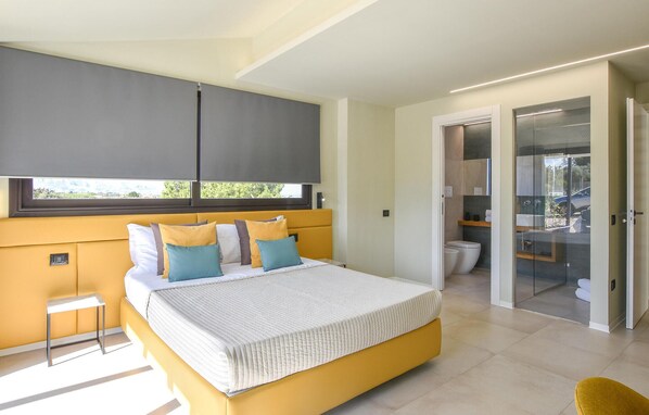 A modern bedroom with a large bed, a bedside table, a wardrobe, and a bathroom visible through a glass door.