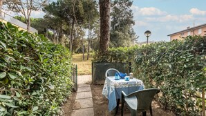 Une terrasse de jardin avec une table dressée pour deux personnes, entourée d’un feuillage dense et d’arbres.