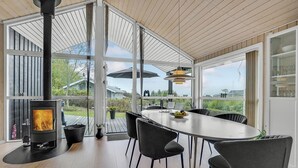 A modern kitchen with a large window, a built-in wood stove, and a dining area with chairs and a table. - Cozy home in Løgstrup with kitchen (Løgstrup)