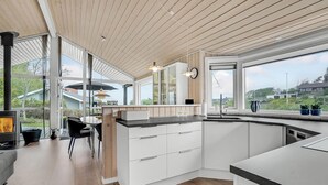 A modern kitchen with white cabinets, a wooden ceiling, and large windows offering views of the surrounding area. - Cozy home in Løgstrup with kitchen (Løgstrup)
