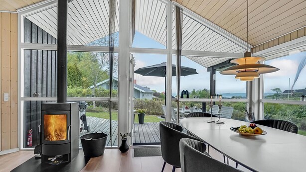 A modern living room with a glass wall, a fireplace, and a dining area with outdoor views. - Cozy home in Løgstrup with kitchen (Løgstrup)