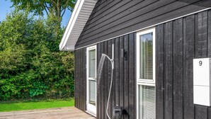 A black building with a number 9 sign, a wooden deck, and a garden with green foliage. - Cozy home in Løgstrup with kitchen (Løgstrup)