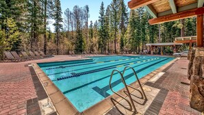 Ein Schwimmbecken mit Bahnteilern, umgeben von einer Ziegelterrasse und einer Holzpergola.