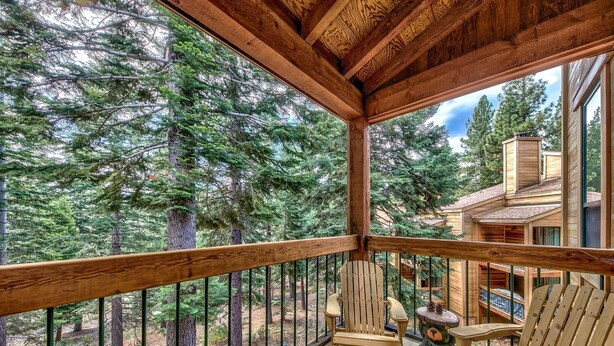 A wooden deck with a view of a forest, a chair, and a table.