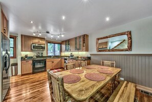 Una cucina moderna con mobili in legno, elettrodomestici in acciaio inossidabile e un ampio tavolo da pranzo con sottopiatti in fibra naturale.