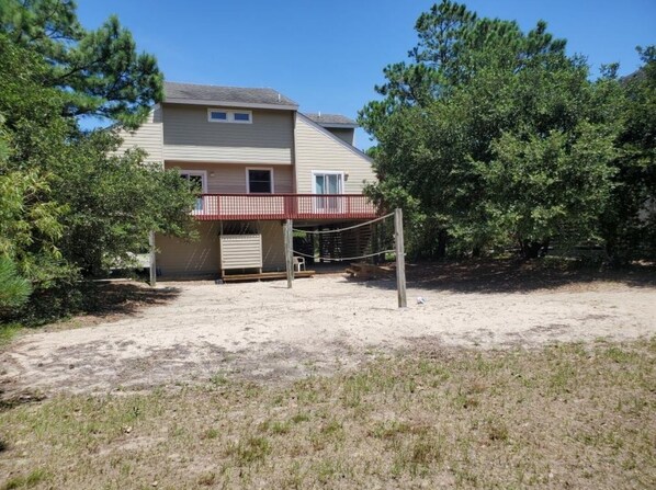 Uma casa de dois andares com uma varanda vermelha e uma rede de voleibol no quintal.
