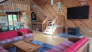 Interior acollidor d'una cabana amb una escala de fusta, una zona de menjador, un sofà i una televisió.