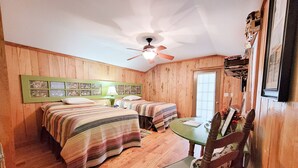 A room with two beds, a ceiling fan, a table with a chair, and wooden walls. - "The DogHouse" a Pet Friendly Cabin on a 70 ac horse farm near Fall Creek Falls! (Van Buren County)