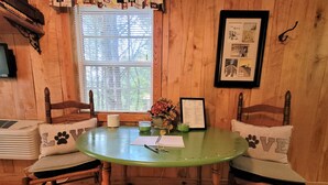 A wooden interior with a round table, two chairs, a window with blinds, and a framed picture on the wall. - "The DogHouse" a Pet Friendly Cabin on a 70 ac horse farm near Fall Creek Falls! (Van Buren County)
