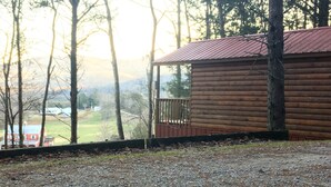 A log cabin with a metal roof, surrounded by trees and a view of a distant building. - "The DogHouse" a Pet Friendly Cabin on a 70 ac horse farm near Fall Creek Falls! (Van Buren County)