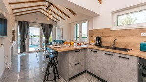 Een moderne keuken met een houten aanrecht, een inbouwoven en een spoelbak. Er is een zithoek met een blauwe bank en een kleine tafel.