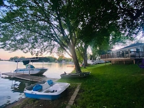A lakeside property with a dock, boats, and a grassy area.