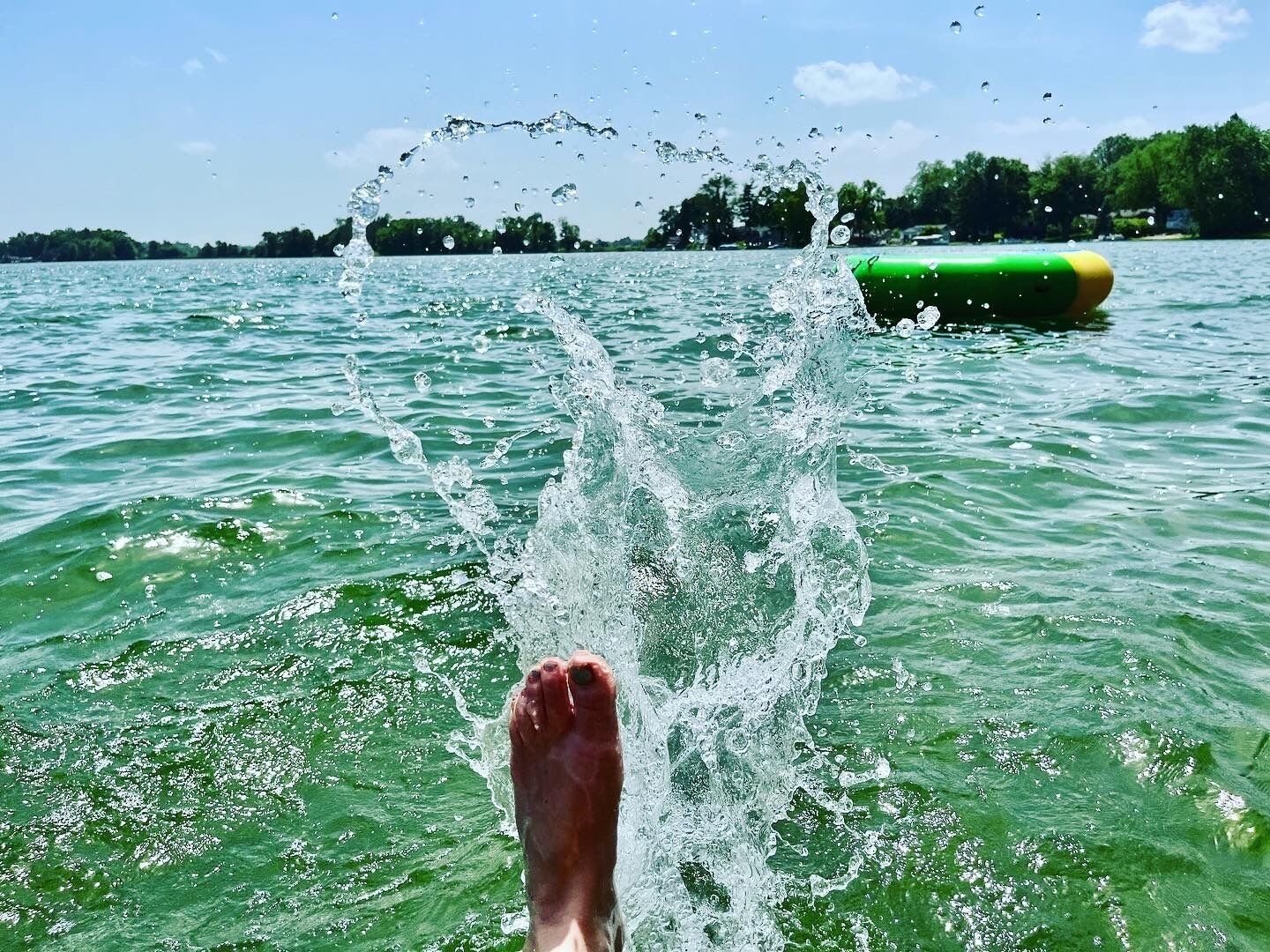 Voet in het water, met een groen voorwerp op de achtergrond.