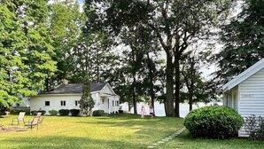 A white house with a front porch, a lawn with a stone pathway, and a large tree in the background.