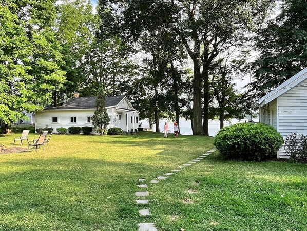 A white house with a front porch, a lawn with a stone pathway, and a large tree in the background.