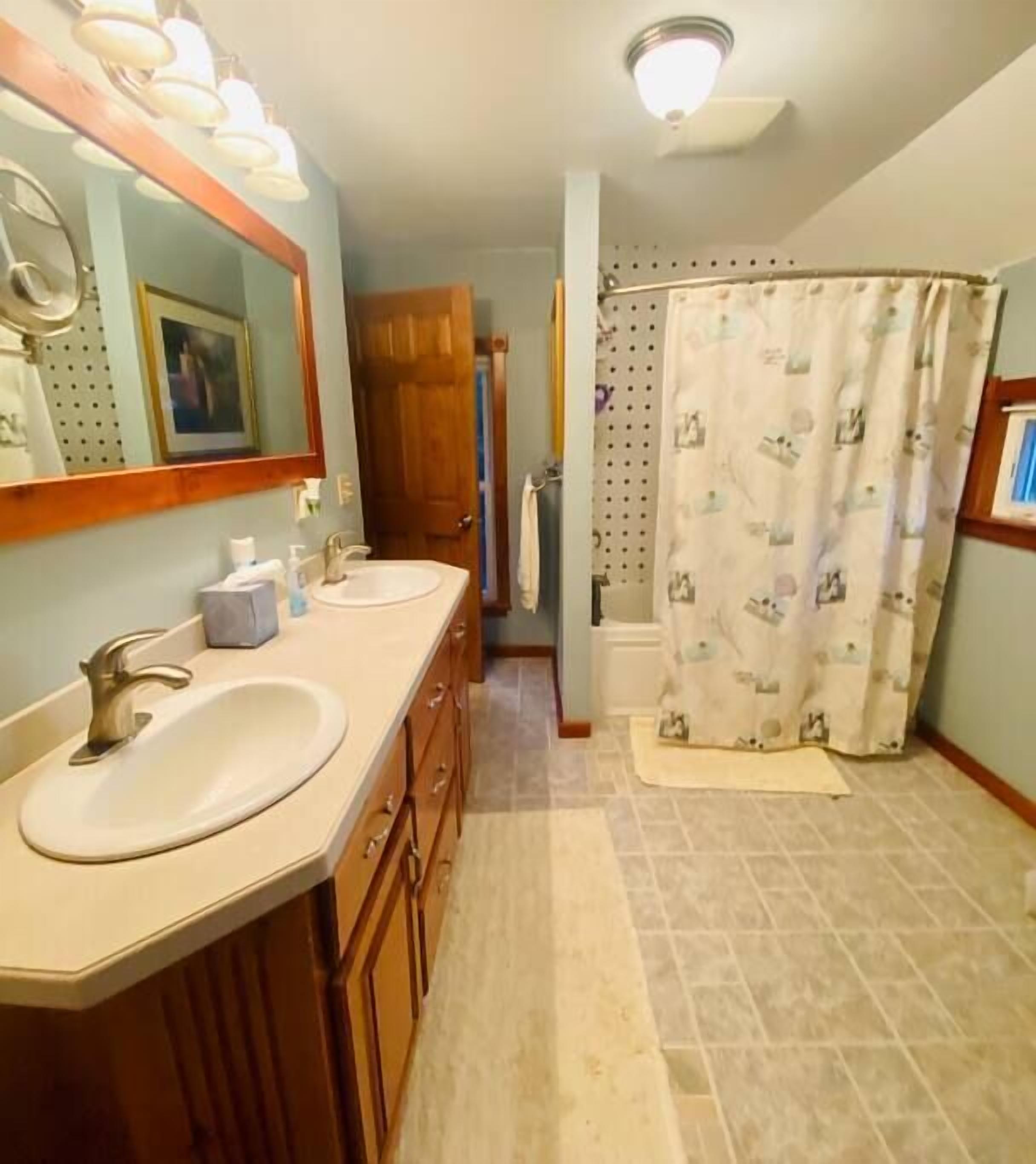 A bathroom with a double sink, wooden cabinets, a mirror, and a shower curtain.