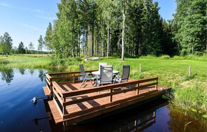 A wooden dock with chairs and a table, surrounded by a forest and a calm body of water. - 1 bedroom awesome home in åmotfors (Åmotfors)