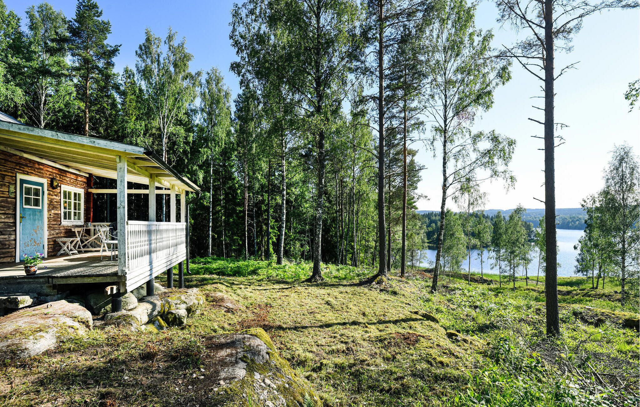 A cabin with a porch and outdoor seating, surrounded by a forest and a lake.