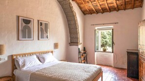 A bedroom with a wooden bed, a stone wall, and a view of greenery outside.